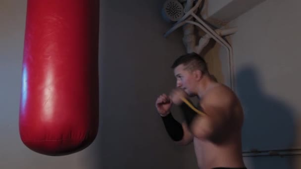 Mužský boxer porazí boxerský pytel v boxerské tělocvičně. — Stock video