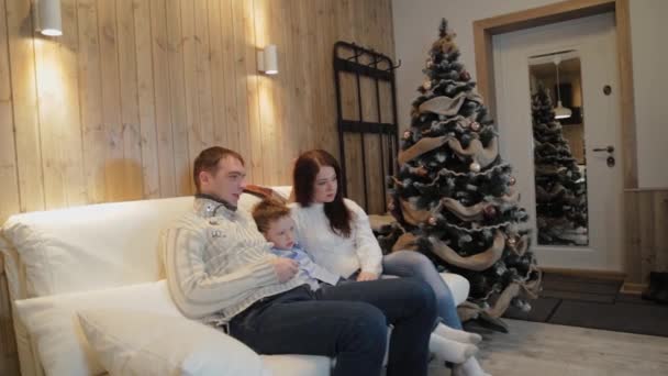 Frumoasă familie fericită de trei pe canapea zâmbind și vorbind lângă pomul de Crăciun în noaptea de Crăciun . — Videoclip de stoc