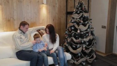 Üç kişilik mutlu bir aile Noel ağacının yanında gülümsüyor ve konuşuyor..