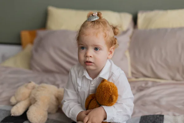 Красивая маленькая девочка на кровати играет с плюшевыми игрушками . — стоковое фото
