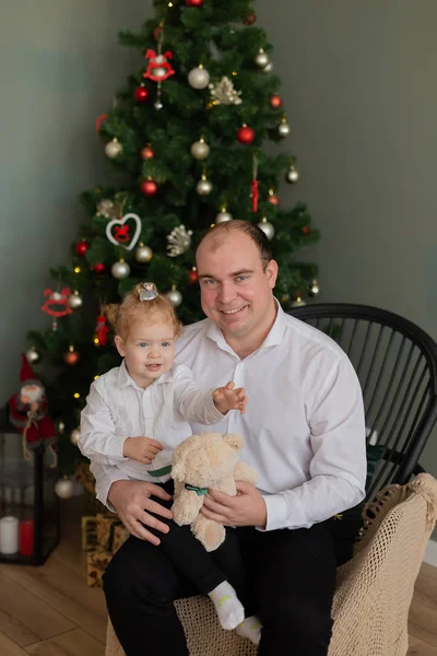 Ein glücklicher Vater mit einer kleinen Tochter im Arm am Weihnachtsbaum. Frohe Weihnachten 2020. — Stockfoto