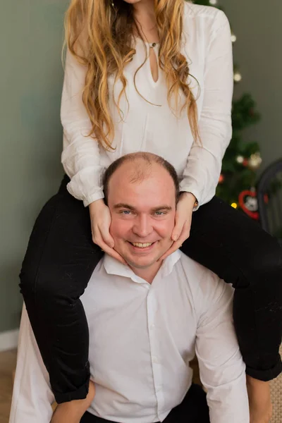 Feliz marido y mujer en el árbol de Navidad en casa. Esposa en marido s espalda . — Foto de Stock