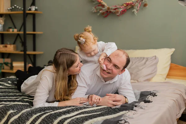 Счастливая семья на современной кровати маленькая дочь кормит папу конфетками . — стоковое фото