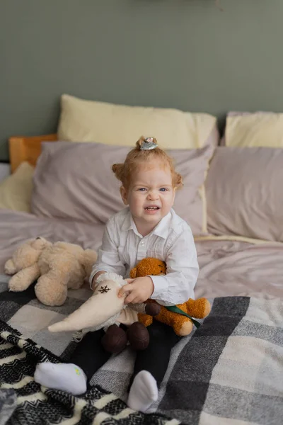 Красивая маленькая девочка на кровати играет с плюшевыми игрушками . — стоковое фото