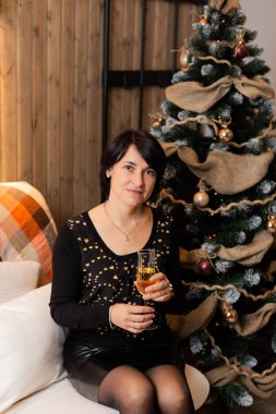 50 yaşında güzel bir kadın yılbaşında bir bardak şampanyayla Noel ağacında. Kadın portresi.