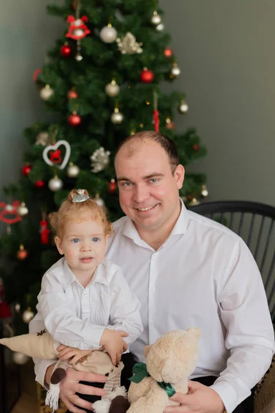 Feliz papá con una pequeña hija en sus brazos en el árbol de Navidad. Feliz Navidad 2020 . — Foto de Stock