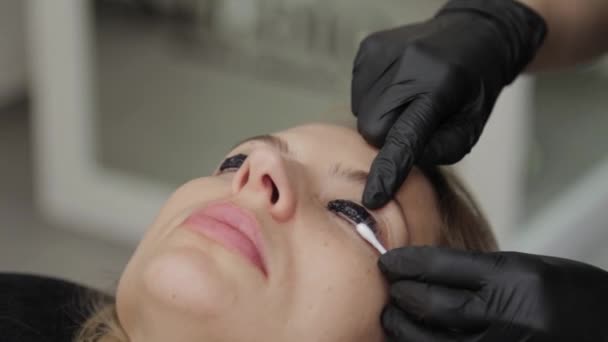 Szakmai kozmetikus egy szépségszalonban szempillákat fest egy ügyfélnek. — Stock videók