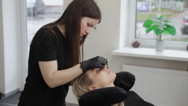 Profesionální kosmetička v salonu krásy narovnává řasy ke klientovi. — Stock video