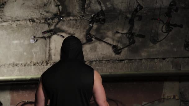 Ein Mann in schwarzer Kleidung blickt mit Bogen und Armbrust an die Wand. — Stockvideo