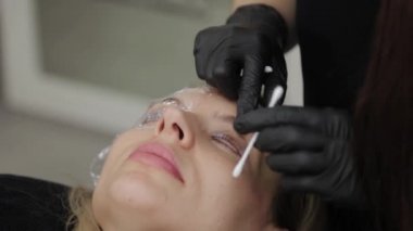 Güzellik salonunda çalışan profesyonel bir güzellik uzmanı müşterisine kirpiklerini boyuyor..