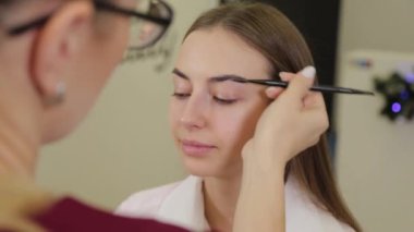 Profesyonel makyöz bir güzellik salonunun müşterisine kaş boyar..