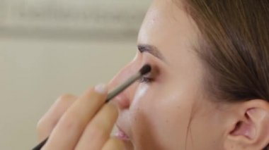 Profesyonel göz makyajı. Makyaj sanatçısı, kuaförde özel fırçası olan genç bir kadına makyaj yapıyor..