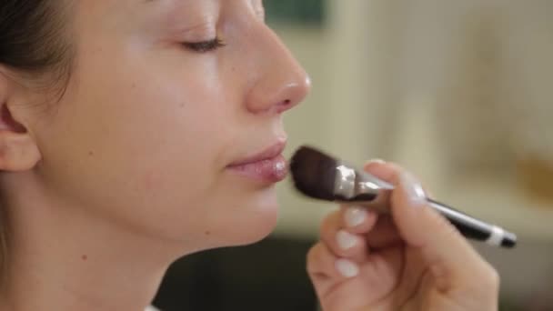 Professionele make-up kunstenaar brengt foundation cream op klanten gezicht met borstel. — Stockvideo