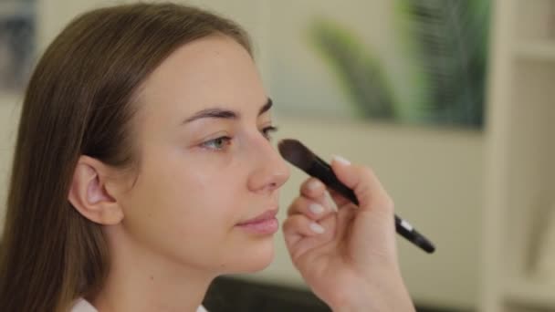 Szakmai make-up művész alkalmazza alapítvány krém az ügyfelek arcát ecsettel. — Stock videók