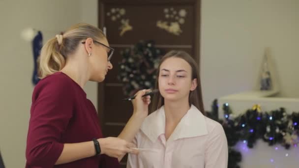 Szakmai make-up művész alkalmazza alapítvány krém az ügyfelek arcát ecsettel. — Stock videók