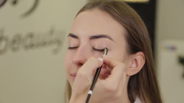 Profesyonel göz makyajı. Makyaj sanatçısı, kuaförde özel fırçası olan genç bir kadına makyaj yapıyor.. — Stok video