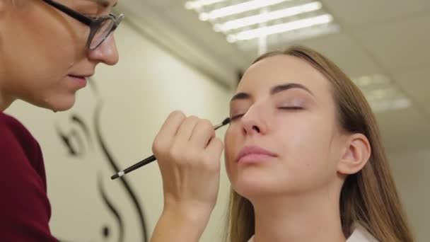 Profesyonel göz makyajı. Makyaj sanatçısı, kuaförde özel fırçası olan genç bir kadına makyaj yapıyor.. — Stok video