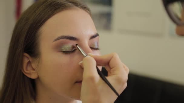 Professionell ögonmakeup. Stylist makeup artist applicerar makeup på en ung kvinna med en speciell borste i en skönhetssalong. — Stockvideo