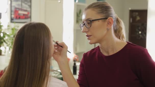 Maquillaje de ojos profesional. Artista de maquillaje estilista aplica maquillaje a una joven con un cepillo especial en un salón de belleza . — Vídeos de Stock