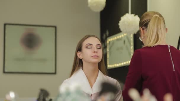 Szakmai sminkes tesz szemhéjpúder egy ügyfél egy szépségszalon. — Stock videók