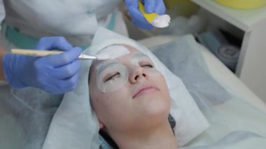 Profesyonel güzellik uzmanı kadın yüz fırçasıyla müşterisine maske takıyor..