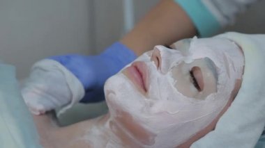 Profesyonel kozmetikçi kadın ıslak mendille müşterilerin yüzündeki maskeyi çıkarıyor..