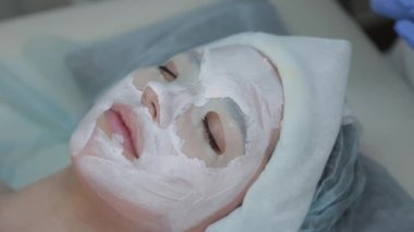 Profesyonel kozmetikçi kadın ıslak mendille müşterilerin yüzündeki maskeyi çıkarıyor..