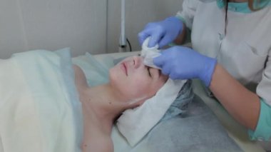Profesyonel kozmetikçi kadın ıslak mendille müşterilerin yüzündeki maskeyi çıkarıyor..