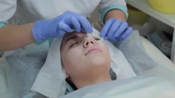 Mujer esteticista profesional aplicando mascarilla facial al cliente . — Vídeos de Stock