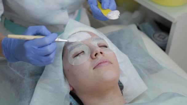 Mujer esteticista profesional aplicando máscara al cliente con cepillo facial . — Vídeos de Stock