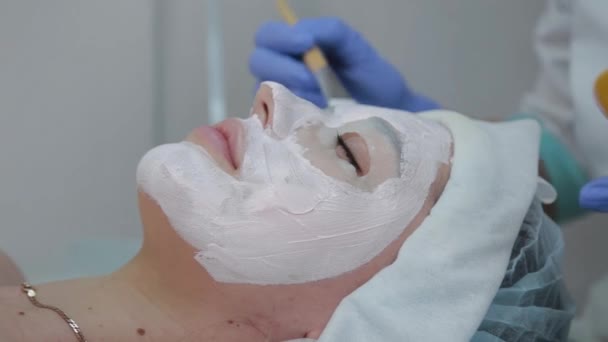 Professionele schoonheidsspecialiste vrouw aanbrengen masker op cliënt met gezicht borstel. — Stockvideo