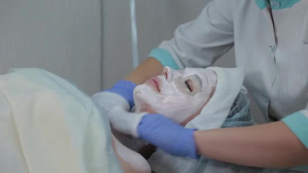 Professional cosmetologist woman removes mask from clients face with wet wipes. — Stock Video