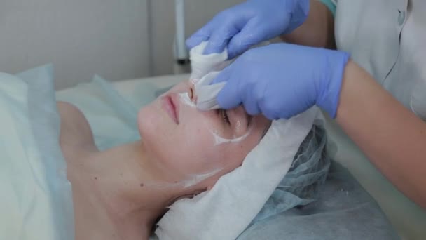 Cosmétologue professionnel femme enlève le masque des clients visage avec des lingettes humides . — Video