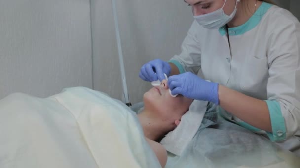 Cosmétologue professionnel femme enlève le masque des clients visage avec des lingettes humides . — Video