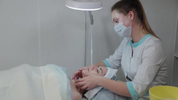 Mujer esteticista profesional realiza masaje facial a la mujer cliente . — Vídeos de Stock