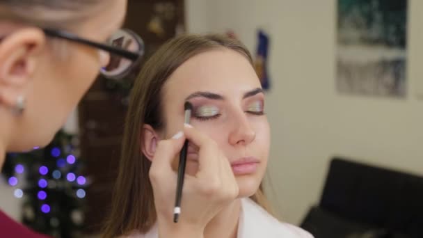 Artista de maquillaje profesional pone sombra de ojos en un cliente de un salón de belleza . — Vídeo de stock
