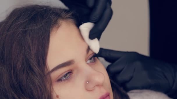 Femme professionnelle maître des sourcils nettoie les sourcils au client dans le salon de beauté . — Video