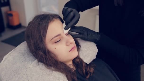 Femme professionnelle maître des sourcils nettoie les sourcils au client dans le salon de beauté . — Video