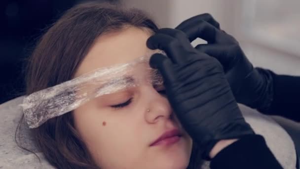 Profesional mujer ceja maestro pone película en las cejas en un salón de belleza . — Vídeo de stock