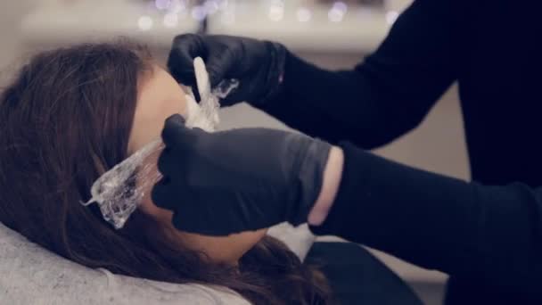 Profissional mulher sobrancelha mestre coloca filme em sobrancelhas em um salão de beleza . — Vídeo de Stock