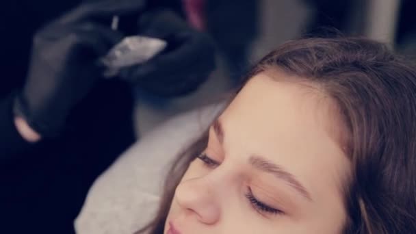 Professional master eyebrow woman removes the film from the eyebrow and removes liquid on the eyebrows in a beauty salon. — Stock Video