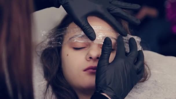 Profissional mulher sobrancelha mestre coloca filme em sobrancelhas em um salão de beleza . — Vídeo de Stock