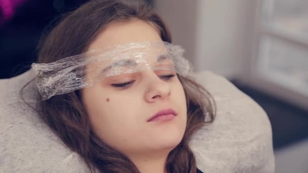 Belle jeune fille avec un film sur les sourcils dans un salon de beauté . — Video