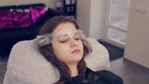 Belle jeune fille avec un film sur les sourcils dans un salon de beauté . — Video