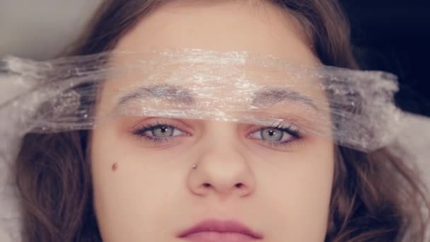 Vacker ung flicka med en film på ögonbrynen i en skönhetssalong. — Stockvideo
