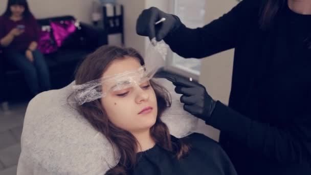 プロのマスター眉の女性は眉からフィルムを削除し、美容室で眉に液体を削除します。. — ストック動画