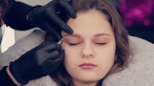 Profesional maestro de cejas mujer arrancando las cejas con pinzas al cliente en el salón de belleza . — Vídeo de stock