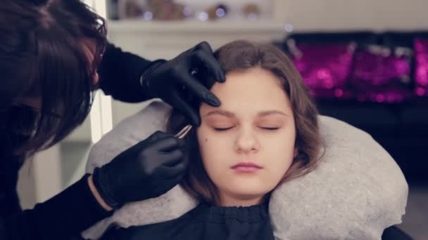 Profesional maestro de cejas mujer arrancando las cejas con pinzas al cliente en el salón de belleza . — Vídeos de Stock