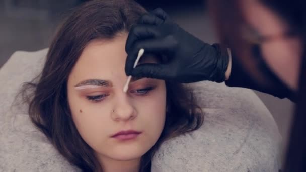 El amo profesional de las cejas de la mujer maneja un brote de algodón con las cejas al cliente en salón de belleza . — Vídeo de stock