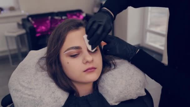El amo profesional de las cejas de la mujer maneja un brote de algodón con las cejas al cliente en salón de belleza . — Vídeos de Stock